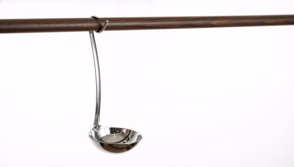 Polished stainless steel ladle hanging on a wooden kitchen rail. Shiny metal soup spoon utensil isolated on white background. Copy space Stainless Steel Soup Ladle